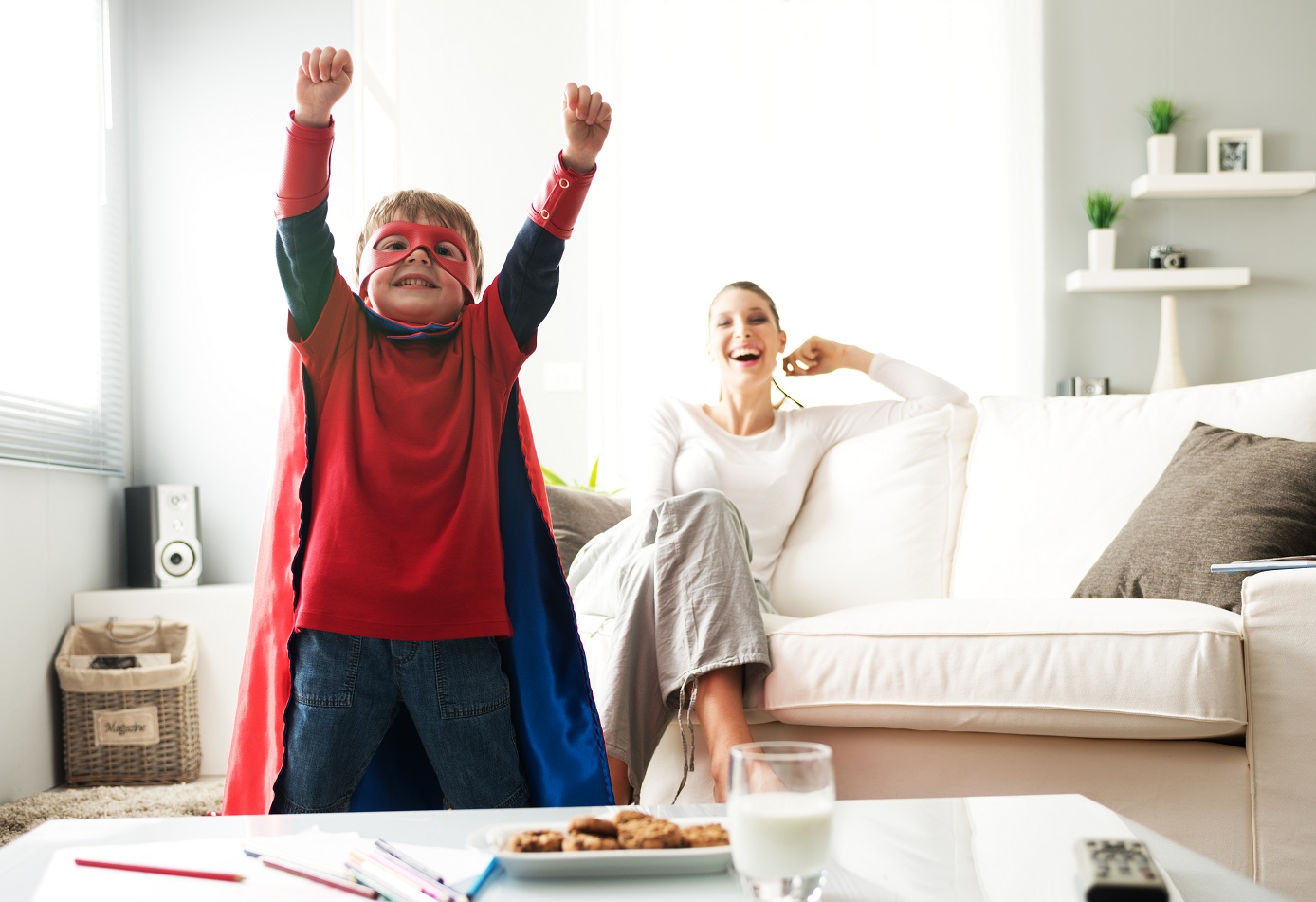 Superhero boy having an healthy snack with cookies and milk with his mother on background.